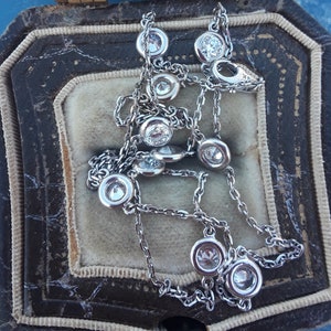 May include: A silver chain necklace with round, bezel-set diamonds. The necklace is in a velvet-lined jewelry box.