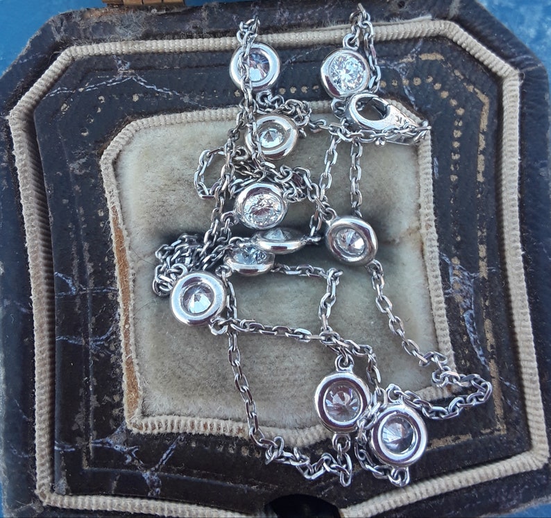 May include: A silver chain necklace with round, bezel-set diamonds. The necklace is in a velvet-lined jewelry box.