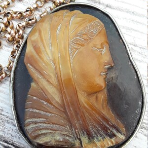 May include: A silver chain necklace with a cameo pendant featuring a carved profile of a woman in a brown and gold shell cameo. The cameo is set in a silver oval frame.