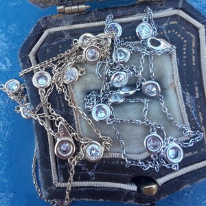 May include: Two delicate silver and gold necklaces with small diamond-like stones. The necklaces are displayed in a velvet-lined jewelry box.