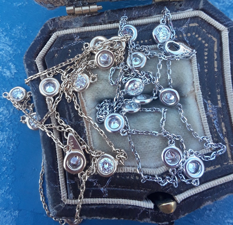 May include: Two delicate silver and gold necklaces with small diamond-like stones. The necklaces are displayed in a velvet-lined jewelry box.