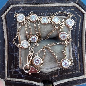 May include: A gold chain necklace with round, bezel-set diamonds. The necklace is in a brown velvet jewelry box.