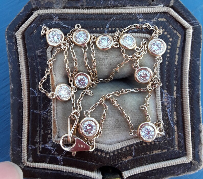 May include: A gold chain necklace with round, bezel-set diamonds. The necklace is in a brown velvet jewelry box.