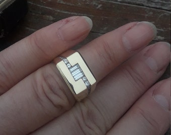 May include: A gold ring with a rectangular setting featuring a row of baguette-cut diamonds and smaller round diamonds around the edges.