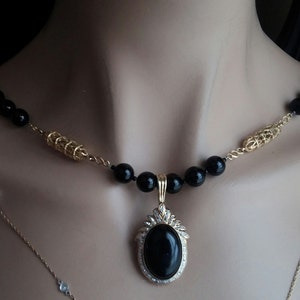 May include: A gold chain necklace with black beads and a large oval pendant with a black stone and clear rhinestones.