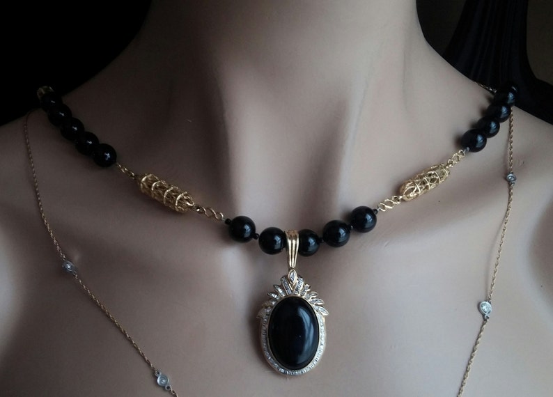 May include: A gold chain necklace with black beads and a large oval pendant with a black stone and clear rhinestones.