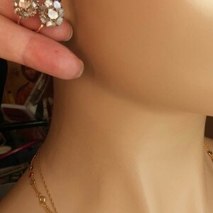 May include: A pair of gold earrings with a cluster of small, clear stones. The earrings are on a mannequin's ear. The mannequin is also wearing a gold necklace with small, colourful stones.