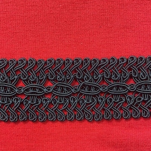 May include: Black braided trim with a decorative pattern. The trim is on a red fabric background.