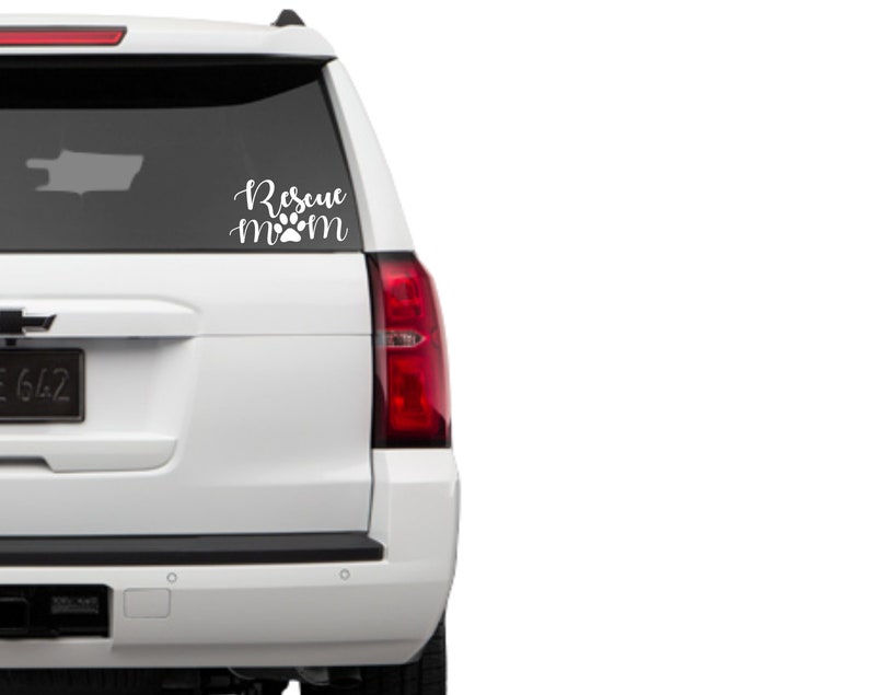 May include: White car window decal with the words "Rescue Mom" in a cursive font, with a paw print replacing the "o" in "mom". The decal is designed to be applied to a vehicle's rear window.