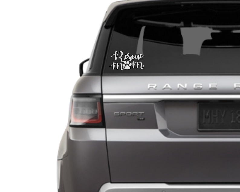 May include: White vinyl car decal with the words "Rescue mom" in a cursive font, with a paw print replacing the "o" in mom. The decal is on the rear window of a silver SUV.