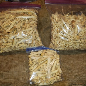 May include: Three bags of white animal bones, likely chicken bones, in various sizes. The bones are in clear plastic bags with zipper closures. The bags are sitting on a brown hessian surface.