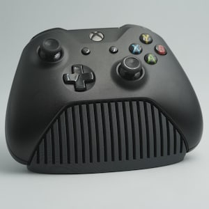 May include: A black video game controller featuring a matte finish, two analogue sticks, a directional pad, and four coloured action buttons labelled A, B, X, and Y. The lower section of the controller has a distinct vertical ribbed texture design.
