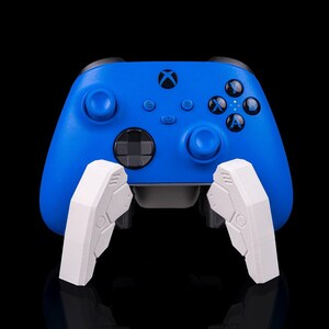 May include: A blue Xbox controller with white attachments. The controller has black buttons and directional pad. The white attachments are angular and designed to fit on the controller.
