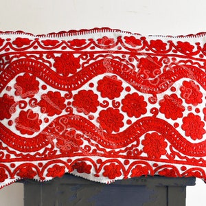May include: White pillow with red embroidered floral pattern. The embroidery features a repeating design of stylized flowers and wavy lines.