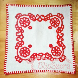 Puede incluir: Cuadrado de lino blanco con un borde bordado en rojo con un diseño floral. El borde tiene un borde festoneado.