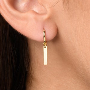May include: Gold hoop earrings with a dangling rectangular charm.