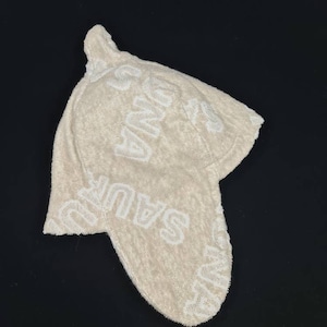 Peut inclure: Un bonnet en tricot beige avec un logo "Sauce" blanc répété sur le tissu.