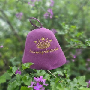 Peut inclure: Un bonnet de sauna en feutre violet avec une couronne dorée et le texte "Saunaprinzessin" brodé sur le devant.