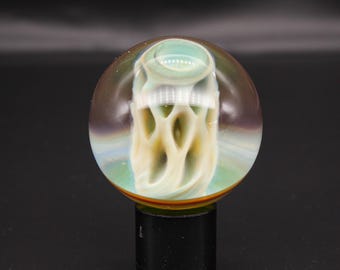 May include: A spherical glass paperweight featuring a clear outer layer and an internal core with swirling cream and pale green organic, web-like patterns. The sphere has a smooth, polished surface and sits atop a dark, cylindrical base.