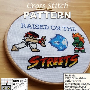 May include: Cross stitch pattern featuring pixelated characters and the text "RAISED ON THE STREETS." The design includes a character throwing a fireball and another character in a fighting stance, all within a wooden embroidery hoop.