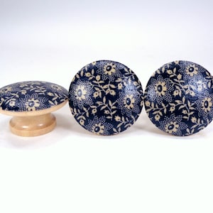 May include: Three wooden knobs with a blue and cream floral pattern. The knobs are round and have a raised edge.