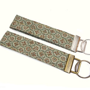May include: Two fabric keychains with a green and brown floral pattern. One keychain has a silver key ring and the other has a bronze key ring.