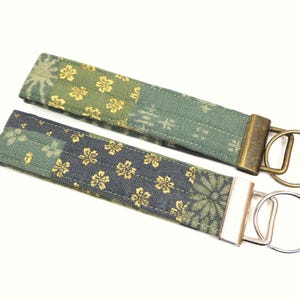 May include: Two fabric keychains with gold and green floral patterns. One keychain has a brass key ring and the other has a silver key ring.