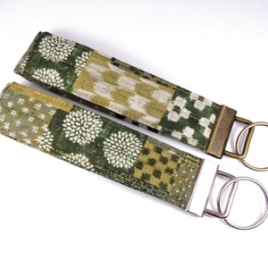 May include: Two fabric keychains with green and gold patterned fabric. One keychain has a brass key ring and the other has a silver key ring.