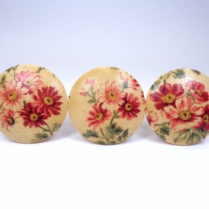 May include: Three round wooden buttons with a floral pattern. The buttons are cream colored with pink and red flowers and green leaves.