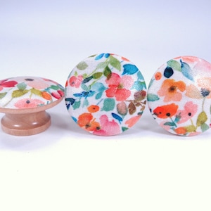 May include: Three round wooden knobs with a white background and a floral pattern in shades of pink, orange, blue, and green.
