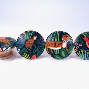May include: Four round wooden knobs with a dark green background and colorful animal illustrations. The knobs feature a tiger, a monkey, a bird, and a leopard.