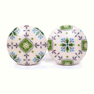 May include: Two round cabinet knobs with a white background. Each knob features a repeating pattern of green, blue, and gray floral designs. The knobs are likely made of fabric or a similar material.