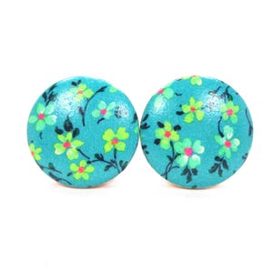 May include: Two round, turquoise wooden earrings with a floral design. Each earring features a pattern of small, lime green and white flowers with black stems and leaves. The earrings are set against a white background.