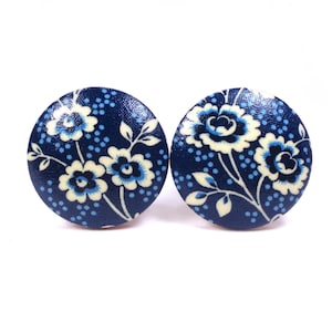 May include: Two circular buttons featuring a dark navy blue background with a repeating pattern of cream-colored flowers, dark blue centers, and small light blue dots. The floral design includes stems and leaves in a cream color across the surface.