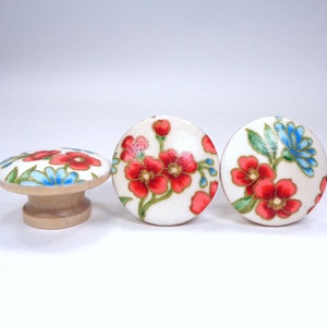May include: Three wooden knobs with a white background and a floral design featuring red, blue, and green flowers. The knobs are round and have a slight shine.