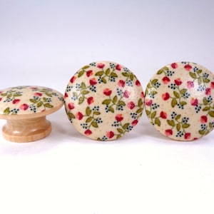 May include: Three wooden knobs with a floral pattern. The knobs are beige with red and green flowers and blue accents.