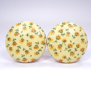May include: Two round cabinet knobs with a floral pattern. The knobs have a cream-colored background with a repeating pattern of small orange and yellow flowers and green leaves. The knobs are likely made of wood.
