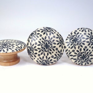 May include: Three decorative cabinet knobs with a floral pattern. The knobs have a cream-colored background with a dark blue floral design. One knob is a mushroom shape, and the other two are round. The bases are made of light-colored wood.