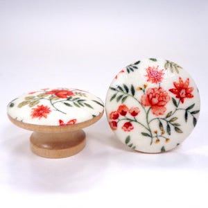 May include: Two round cabinet knobs with a light wood base and a white fabric top featuring a printed floral pattern in shades of red, orange, and green. One knob is shown from the side, while the other is positioned upright to show the design.