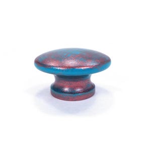 May include: A decorative cabinet knob with a distressed finish. The knob features a teal and reddish-brown color scheme. The knob has a rounded top and a cylindrical base, perfect for adding a touch of rustic charm to furniture.