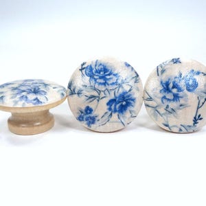May include: Three wooden knobs with a white background and blue floral pattern. The knobs are round and have a raised edge.