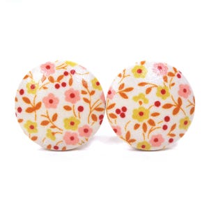 May include: Two circular fabric-covered buttons featuring a white background with a repeating pattern of small pink and yellow flowers, orange leaves, and tiny red berries. The buttons have a smooth, rounded surface and a consistent floral print.