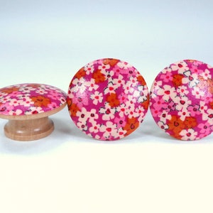 May include: Three wooden knobs with a pink and orange floral pattern. The knobs are round and have a flat top.