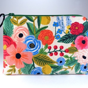 May include: A white zippered pouch with a floral print featuring red, pink, blue, yellow, and green flowers. The pouch has a black drawstring.