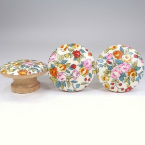May include: Three round wooden knobs with a floral pattern. The knobs are white with pink, orange, yellow, and green flowers. The knobs are about 1 inch in diameter.