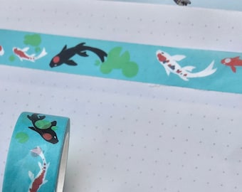 Könnte beinhalten: Eine Rolle türkisfarbenes Washi-Tape mit einem sich wiederholenden Muster aus schwarzen und weißen Koi-Fischen, roten und weißen Koi-Fischen und grünen Seerosen.