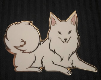 May include: A white dog enamel pin with gold trim. The dog is lying down with a curled tail and a smiling expression. The pin has a smooth, glossy finish and is set against a dark background.