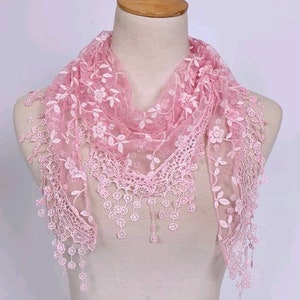 Peut inclure: Écharpe en dentelle rose clair ornée de motifs floraux et de feuilles. L'écharpe est drapée sur un mannequin et présente des franges délicates et une forme triangulaire. La dentelle est ornée de petites fleurs et de feuilles.