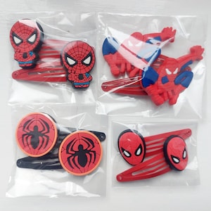 May include: Four sets of Spider-Man themed hair clips in clear plastic packaging. Each set features different designs, including the Spider-Man mask and spider symbols, in red, black, blue, and white. The clips are red.