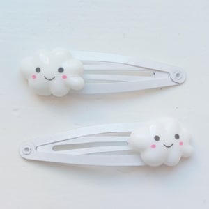 Op de afbeelding: Twee witte plastic haarclips met een glimlachend wolkontwerp. Elke clip heeft drie tanden om haar vast te houden.